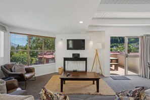 A modern living room with a large window, a flat-screen TV, a wooden coffee table, and a sofa. - Peaks & Cranbury 17B:  Location & Views ! (Queenstown)