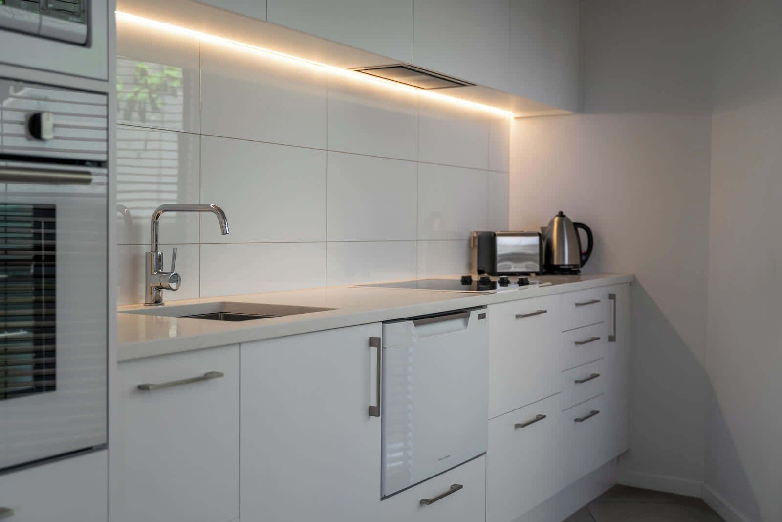 Une cuisine moderne avec des meubles blancs, un évier en acier inoxydable, un grille-pain et une bouilloire.