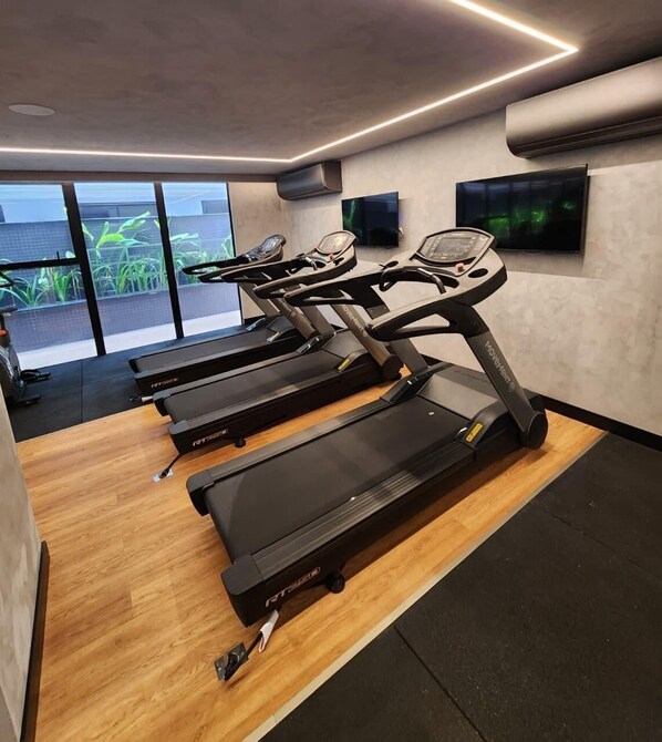 A gym with multiple treadmills, a wooden floor, and large windows with a view of greenery. - HIT Cabo Branco (João Pessoa)