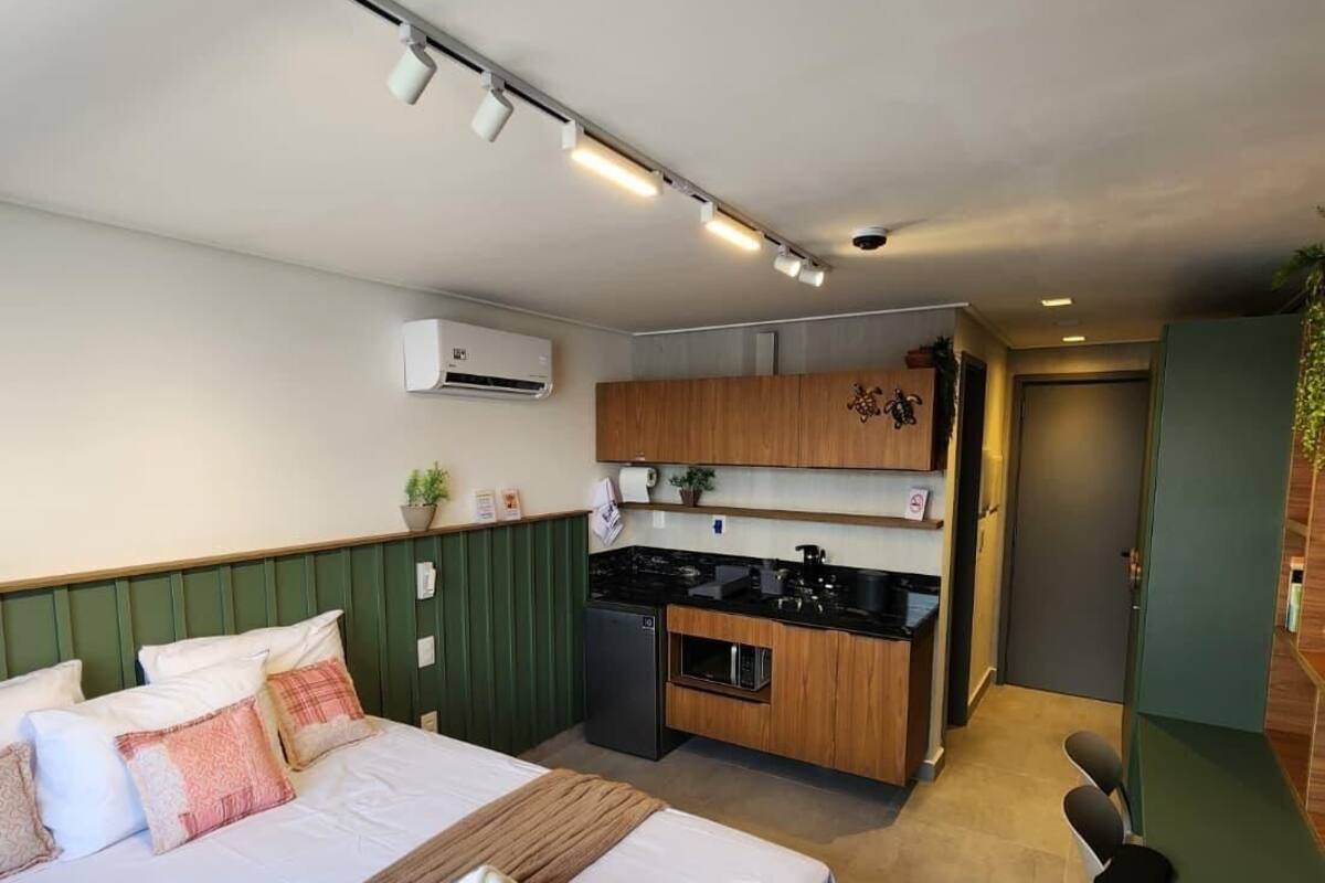 A bedroom with a bed, pillows, a blanket, a small kitchenette, and a bathroom.