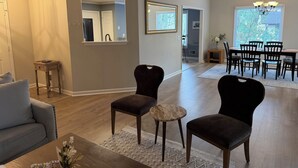 A living room with a gray sofa, two dark armchairs, a coffee table, and a dining area with a table and chairs. - Stylish 3 BR home in Downtown Lexington (Lexington)