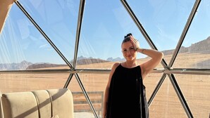 Ein Zimmer mit großem Fenster, einem beigen Sofa, einem kleinen roten Tisch und einem gemusterten Teppich.