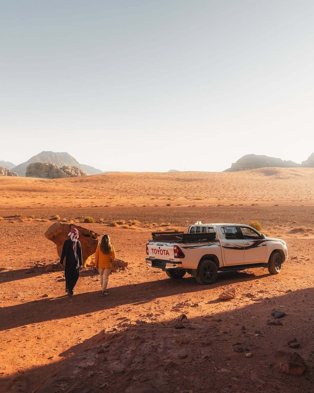 A desert landscape with a white Toyota pickup truck parked on the sand.