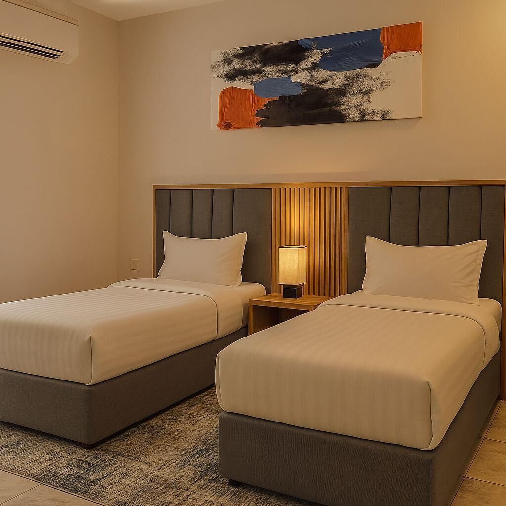 Een hotelkamer met twee bedden, een houten hoofdbord, een nachtkastje met een lamp en een schilderij aan de muur.