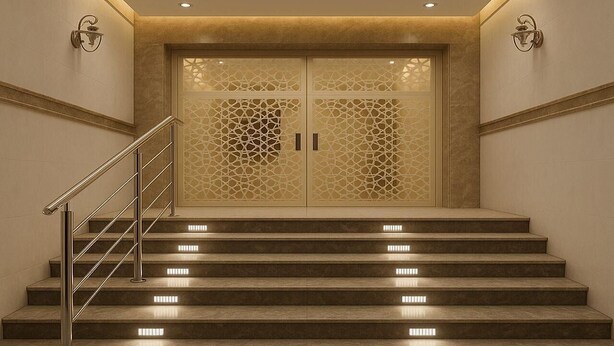 Um conjunto de degraus de mármore com guarda-corpo de metal que levam a uma porta dupla com desenhos geométricos detalhados.
