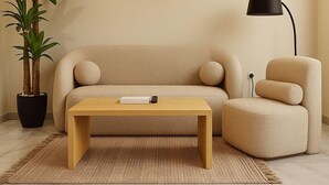 Uma sala de estar com um sofá bege, uma mesa de centro de madeira, um abajur preto e um vaso de planta.