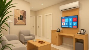 Quarto de hotel moderno com sofá, mesa de centro, escrivaninha, televisão e cozinha compacta.