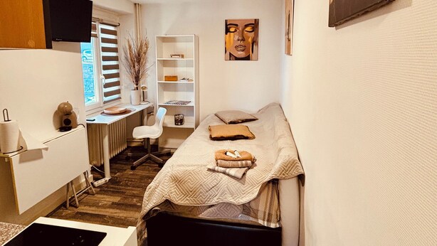 Quarto compacto com uma cama, uma escrivaninha e uma cadeira.