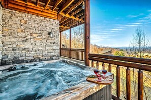 A hot tub with a wooden deck, stone wall, and a scenic view. - Valley Views | Hot Tub, Sauna, Game Room | Sleeps 14 (Sevierville)