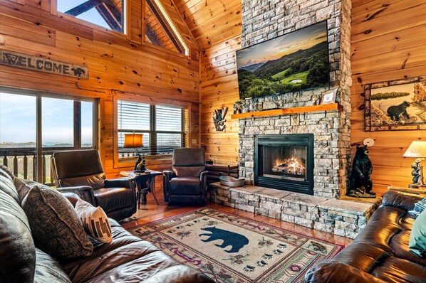 A log cabin interior with a stone fireplace, leather furniture, and a 'Welcome' sign. - Valley Views | Hot Tub, Sauna, Game Room | Sleeps 14 (Sevierville)