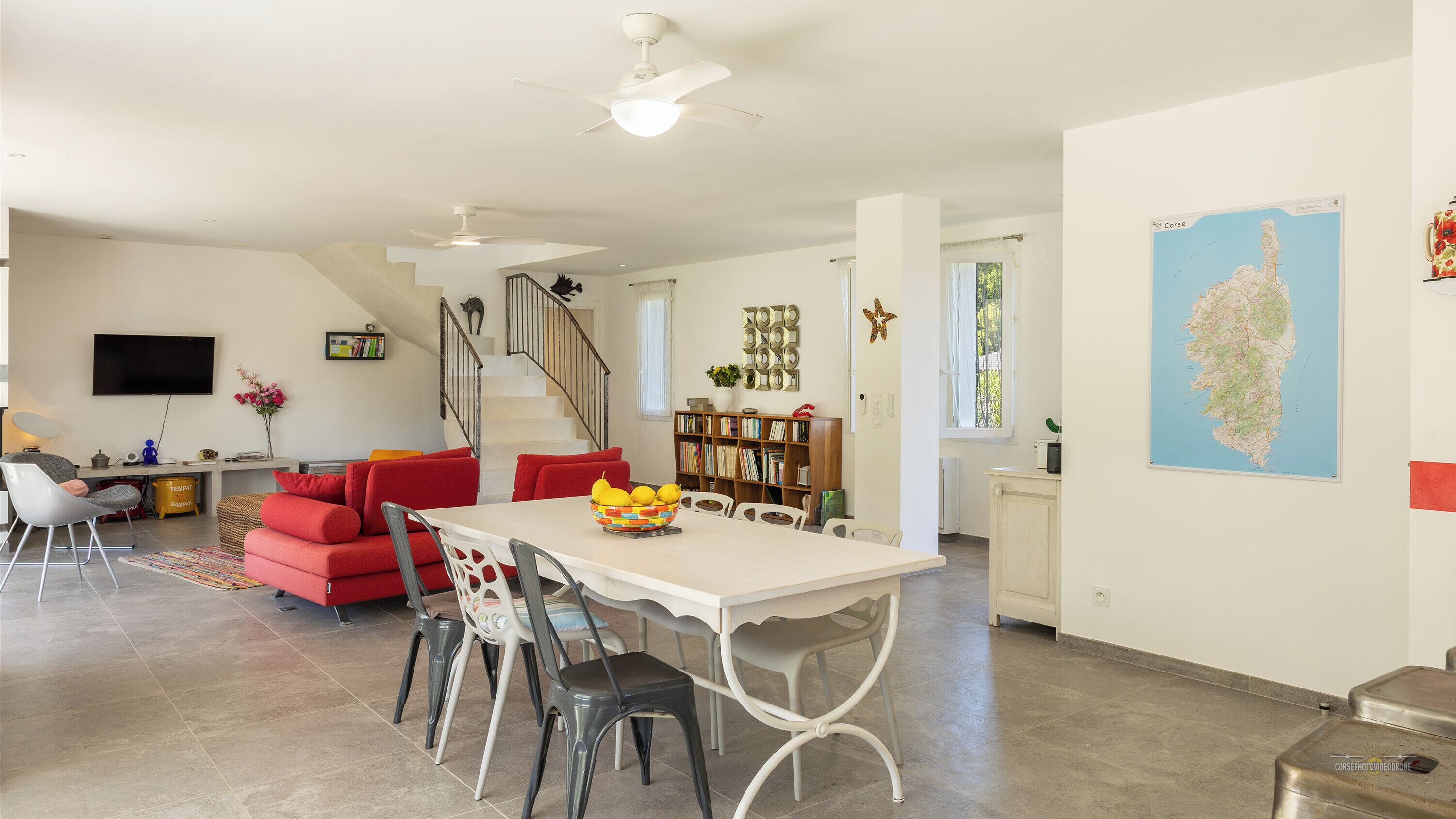 A spacious living area with a dining table, red sofa, and a staircase leading to another level.