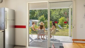 Une cuisine moderne équipée d’un réfrigérateur, un coin repas avec une table et des chaises, et une porte-fenêtre coulissante donnant sur un jardin.