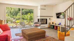 Una sala de estar con sofá, reposapiés y sillones, chimenea, televisor y escalera.