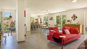 Un vaste espace de vie comprenant un canapé rouge, une table à manger et une cuisine en arrière-plan.
