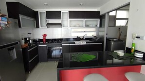 A modern kitchen with black and white cabinetry, a central island with bar stools, and a stainless steel refrigerator.