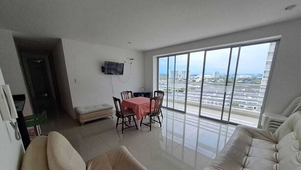 A spacious living room with a large window, a dining area with a table and chairs, and a sofa.