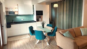 A modern kitchen with white cabinets, a dining table with teal chairs, and a beige sofa with a green pillow. - Cosy Apartment in Espiche near Praia da Luz (Luz)