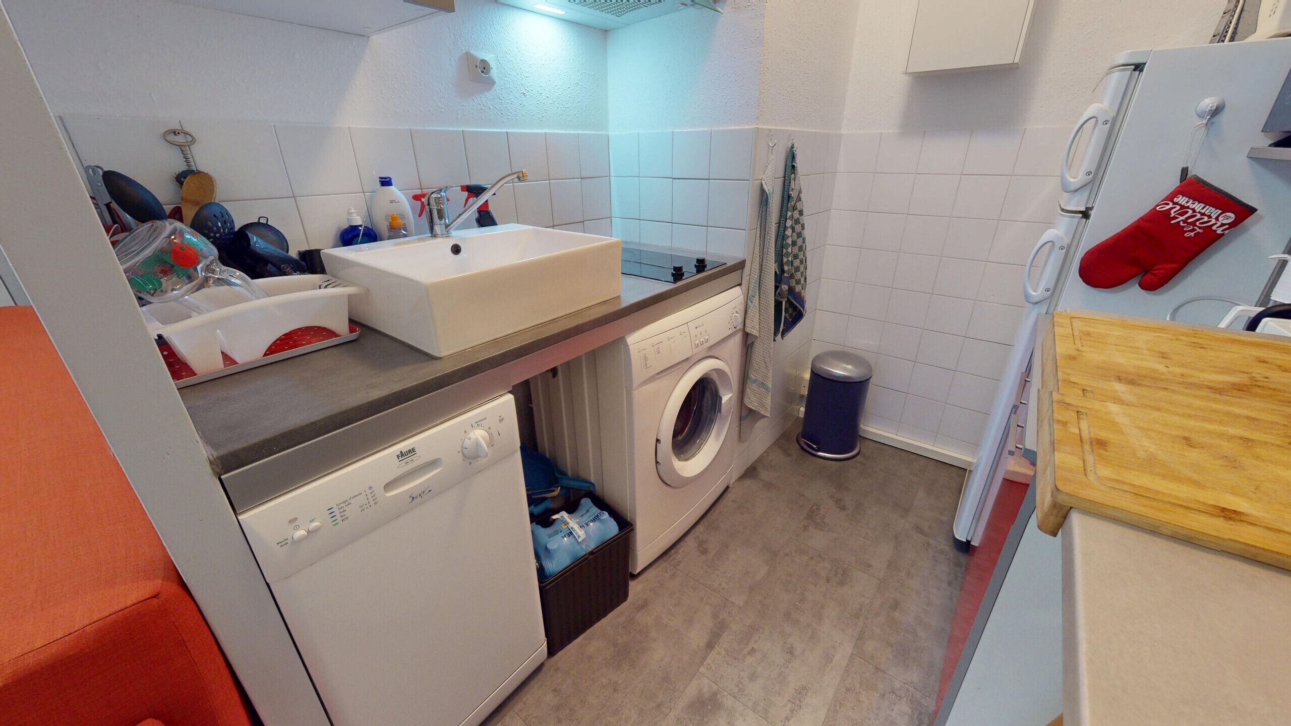 Ett kompakt kök med en diskho, tvättmaskin och en liten papperskorg.