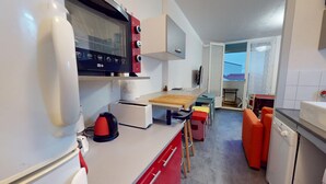 Een praktische keuken met een broodrooster, waterkoker en magnetron. Er is een klein zithoekje met een tafel en stoelen.