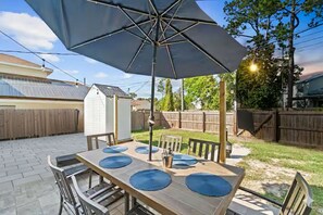 Eine Terrasse mit Tisch für vier Personen, einem Sonnenschirm und einem Holzzaun im Hintergrund.