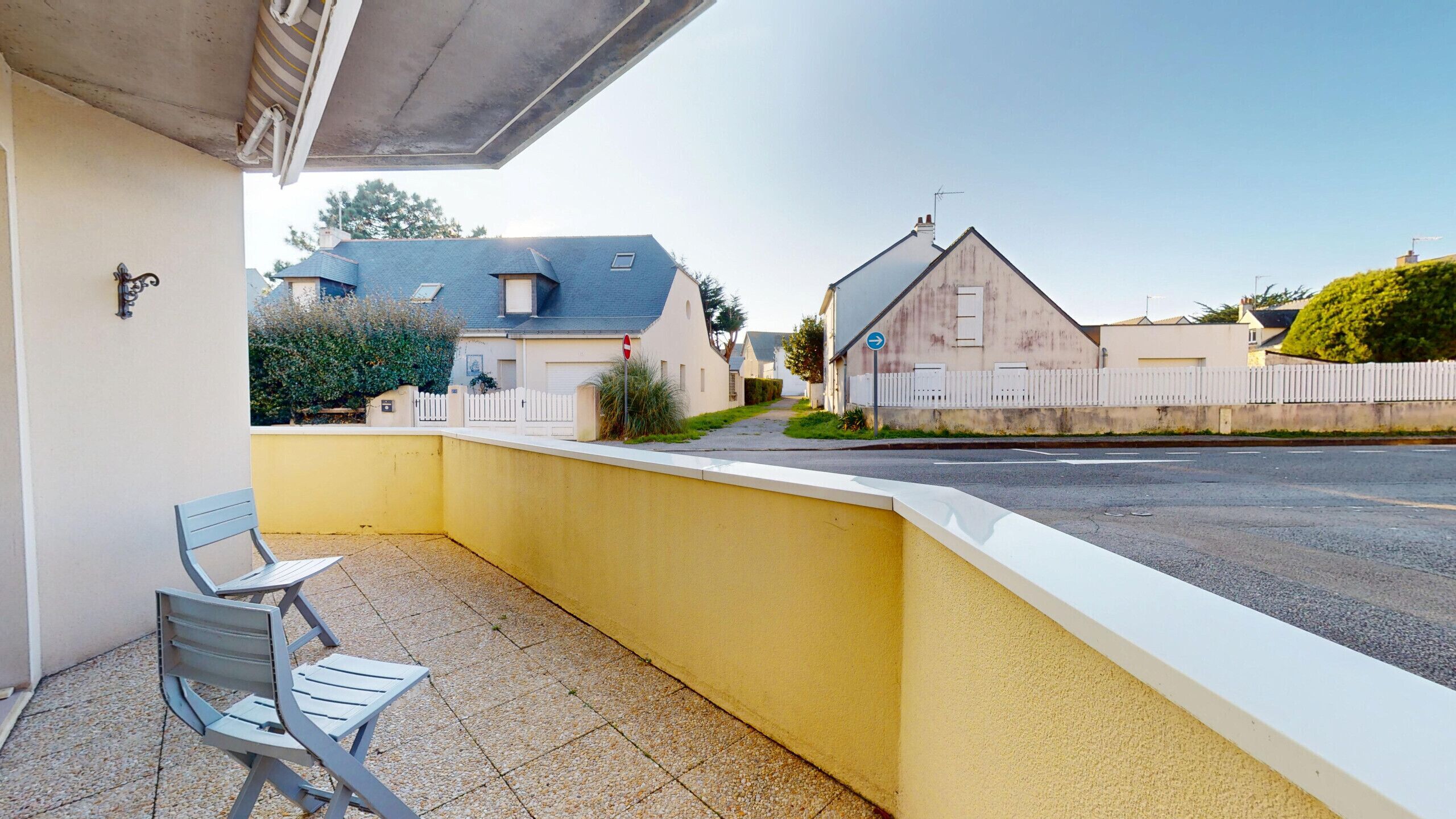A residential street with houses, a white picket fence, and a yellow wall.