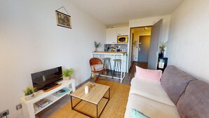 Ein kompakter Wohnbereich mit Fernseher, Sofa, Couchtisch und einer kleinen Küchenzeile mit Barhocker.