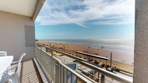 A balcony with a view of a beach, outdoor seating, and a sign indicating a restaurant. - Whisper of the Waves - Oceanfront Studio with Balcony (Saint-Gilles-Croix-de-Vie)