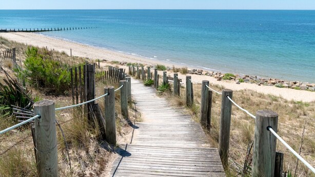 A wooden boardwalk leading to a beach with a wooden fence and rope barrier. - Whisper of the Waves - Oceanfront Studio with Balcony (Saint-Gilles-Croix-de-Vie)