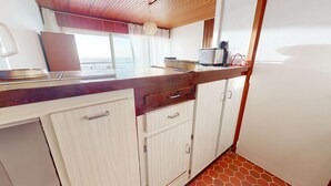 A kitchen with a wooden countertop, white cabinets, and a view of the sea through a window. - Whisper of the Waves - Oceanfront Studio with Balcony (Saint-Gilles-Croix-de-Vie)