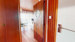 A wooden door with a round mirror, leading into a room with a tiled floor and a bed. - Whisper of the Waves - Oceanfront Studio with Balcony (Saint-Gilles-Croix-de-Vie)
