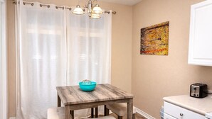 Una cocina pequeña con una mesa de madera, un cuenco azul, un tostador y un cuadro en la pared.
