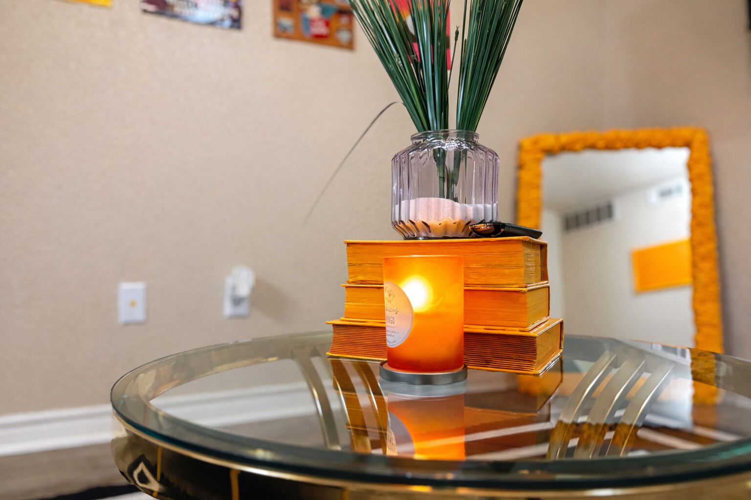 Une table en verre sur laquelle sont posés une bougie allumée et un vase rempli de plantes vertes.