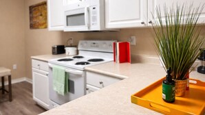 Una cocina con armarios blancos, microondas, estufa y una pequeña planta sobre una bandeja.