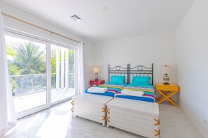 Ein Schlafzimmer mit einem Bett, zwei Nachttischen, einem Fenster mit Blick auf Palmen und einem Deckenventilator.