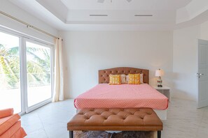 Quarto com uma grande porta de vidro deslizante, cama com cabeceira marrom e um banco.