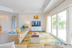 A modern living room with a sofa, TV, and a colorful rug. - Love Beach W2 - Luxury Oceanfront Condo + Pool (Nassau)