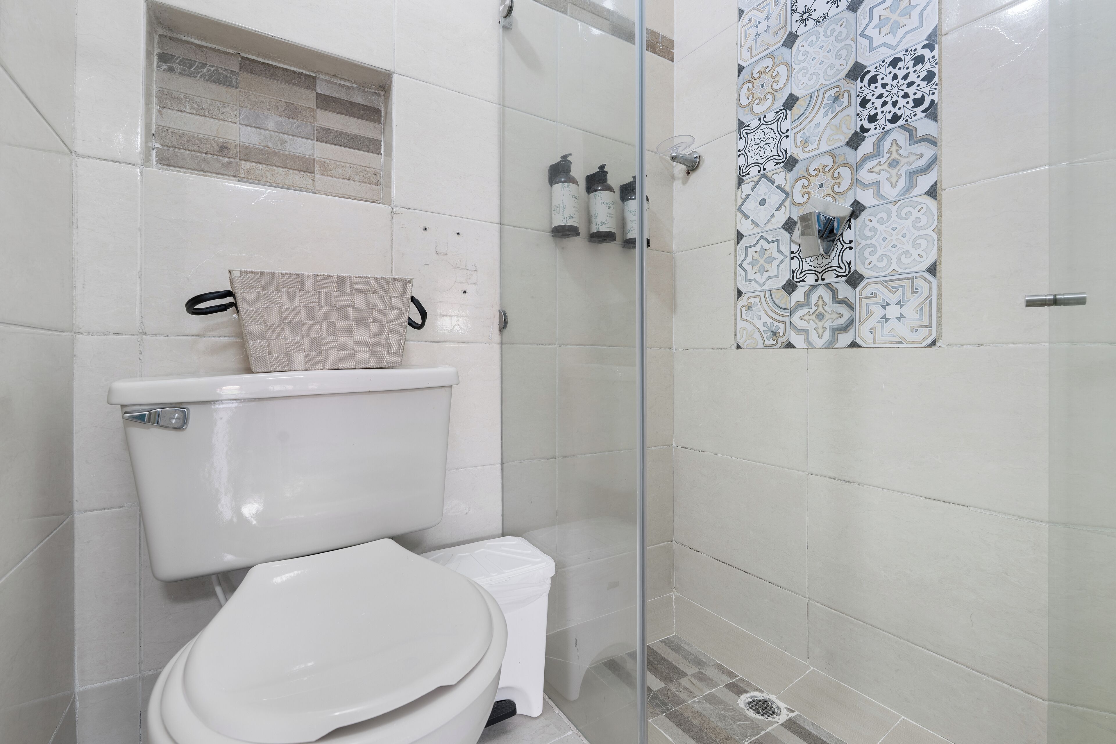 A bathroom with a toilet, a shower enclosure, and a tiled wall with a decorative pattern.