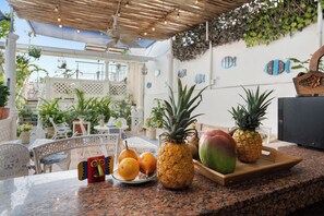 A tropical outdoor dining area with a wooden table, chairs, and a variety of fruits including pineapples and mangoes. - Casa Nueve -Charming 9BR House w/ Pool on Rooftop in the Old City (Cartagena de Indias)