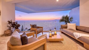 Una sala de estar moderna con un gran ventanal con vistas al mar, amoblada con un sofá, sillas y una mesa de centro.
