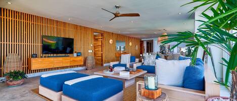 A modern living room with a large TV, blue sofas, wooden paneling, and a ceiling fan.