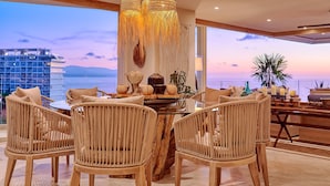 Un comedor moderno con sillas de mimbre, una mesa redonda y vista al océano al atardecer.