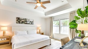 A bedroom with a bed, bedside tables, a desk, a ceiling fan, a window with curtains, and a large plant. - Walk to the beach at Jo Jo's Beach Getaway! (Panama City Beach)