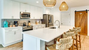 A modern kitchen with white cabinetry, stainless steel appliances, a large island with bar stools, and a wooden barn door. - Walk to the beach at Jo Jo's Beach Getaway! (Panama City Beach)