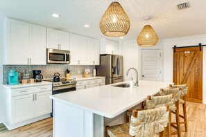 A modern kitchen with white cabinetry, stainless steel appliances, a large island with bar stools, and a wooden barn door. - Walk to the beach at Jo Jo's Beach Getaway! (Panama City Beach)