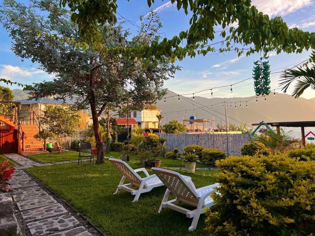 A garden with a paved walkway, a tree, and two white lounge chairs.