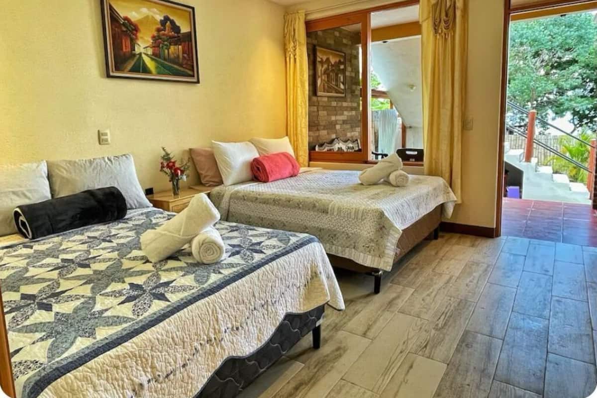 Habitación de hotel con dos camas, un ventanal con cortinas y vista a una escalera que da al exterior.