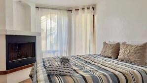 A bedroom with a bed, a fireplace, and a large window with curtains. - Puerto Nuevo Villa Las Conchas 2BR 2 BA with pool (Centro Turístico El Pescador)