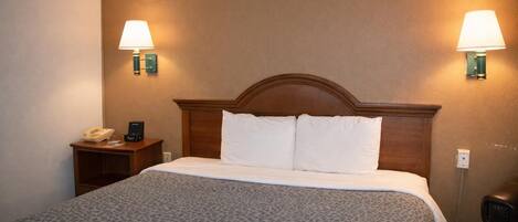 A hotel room with a wooden headboard, a patterned bedspread, two bedside lamps, a telephone, and a nightstand.