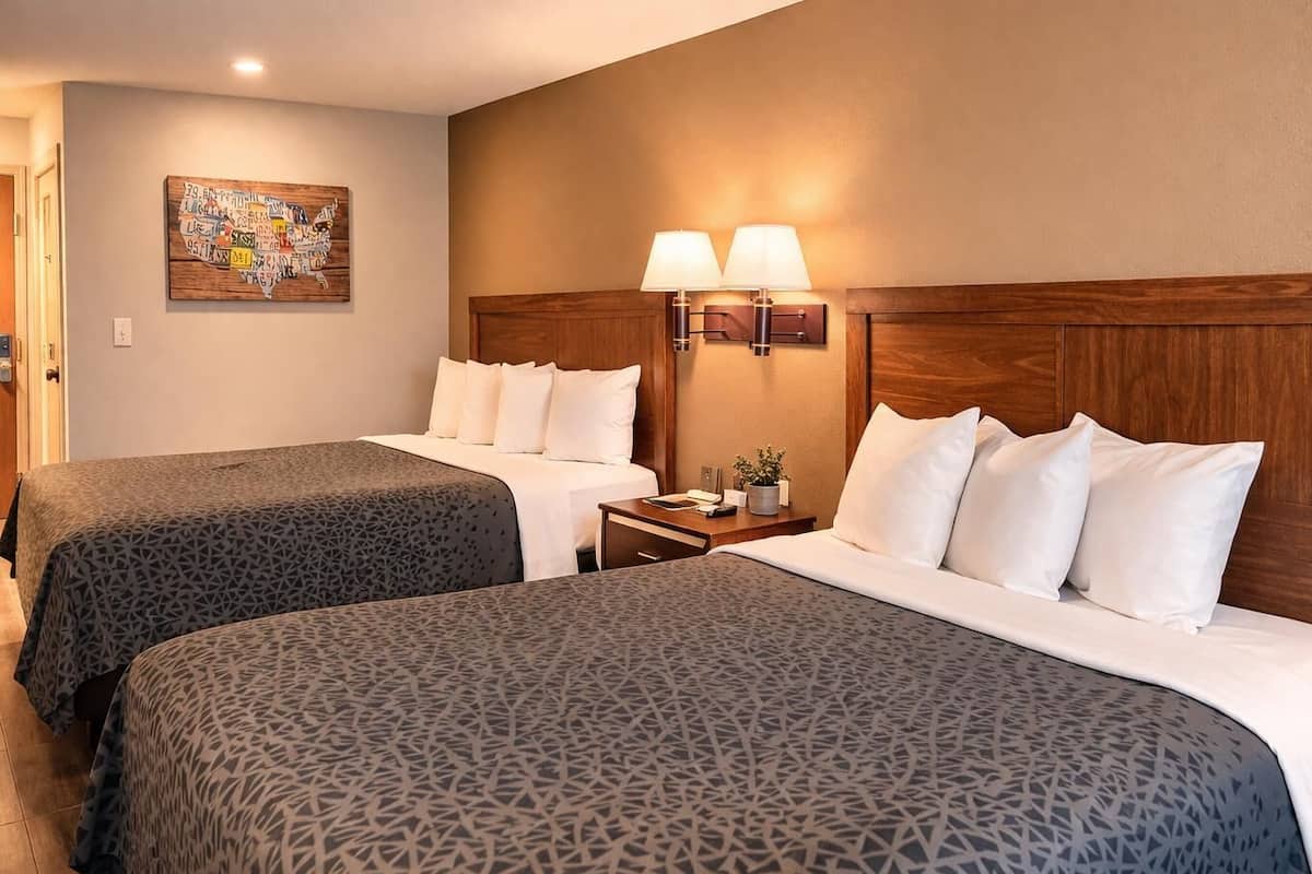 Une chambre d’hôtel avec deux lits, une table de chevet avec des lampes, une carte géographique accrochée au mur et une porte.