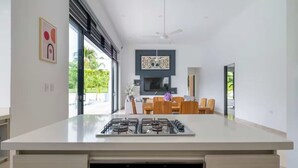 A modern kitchen with a central island, a dining area with wooden chairs, and a large window providing a view of greenery. - Modern Mediterranean style house in Melgar condominium (Carmen de Apicala)